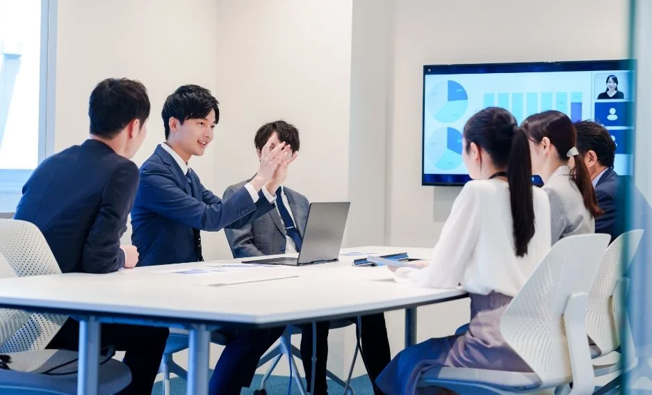 男女6名の社員がモニターに移された円グラフを見ながら会議をしている写真
